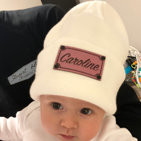 Shop online for beanies and snapback hats from LB Threads for babies, toddlers, kids and adults. Infant model wearing our Cream Custom Name Beanie, a warm, soft, cream-colored acrylic beanie with a leather engraved custom name patch attached with rivets.