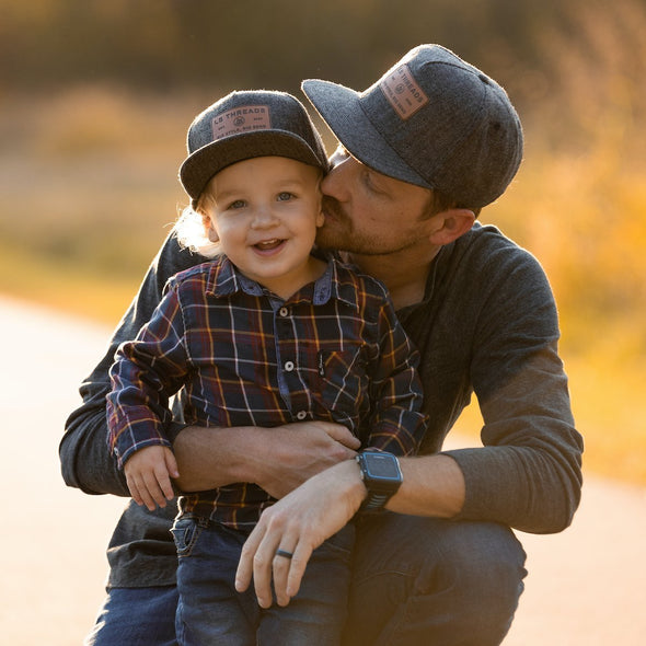 Shop online for snapback hats from LB Threads for baby, toddler, kid and adult. Father and son models wearing the LB Threads Jackson hat, a classic, charcoal herringbone-patterned, wool-blend snapback hat with a brown leather, rectangular LB Threads Big Style, Big Send patch.