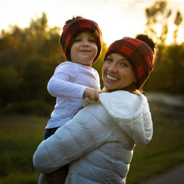 Shop online for beanies and snapback hats from LB Threads for babies, toddlers, kids and adults. Mother and son models wearing the LB Threads Red Buffalo Pom Beanie, a cozy, soft red buffalo plaid topped with a black faux-fur pom, lined with super soft black minky fleece for extra warmth.