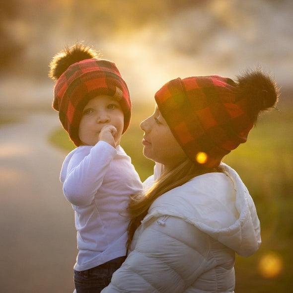 Shop online for beanies and snapback hats from LB Threads for babies, toddlers, kids and adults. Mother and son models wearing the LB Threads Red Buffalo Pom Beanie, a cozy, soft red buffalo plaid topped with a black faux-fur pom, lined with super soft black minky fleece for extra warmth.