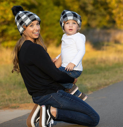 Shop online for beanies and snapback hats from LB Threads for babies, toddlers, kids and adults. Mother and son models wearing the LB Threads White Buffalo Pom Beanie, a cozy, soft white buffalo plaid topped with a black faux-fur pom, lined with super soft black minky fleece for extra warmth.